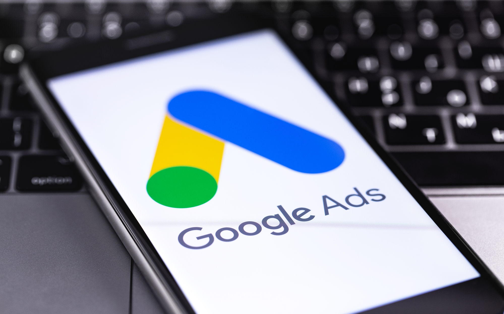 Google Ads symbol on the screen smartphone with notebook closeup